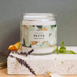 Jar of 'Revive' bath salts with a decorative label on a stone surface.