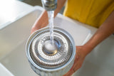 Person washing The Sprouter under running water in a sink