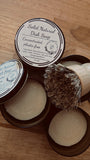 Solid natural dish soap in a container with a brush on a wooden surface