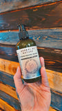Hand holding a bottle of 'Herbal by Nature' magnesium lotion against a wooden background