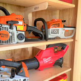 Three power tools on a wooden shelf: two Stihl chainsaws and one Milwaukee tool.