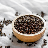 Wooden bowl filled with black peppercorns on a white fabric background