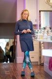 Woman in a kitchen wearing a blue dress and patterned leggings.