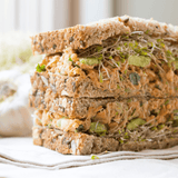 Stack of sandwiches with avocado and sprouts on whole grain bread.