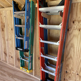 Three ladders of different colors leaning against a wooden wall.
