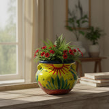 Colorful ceramic vase with plants on a wooden surface near a window