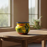 Decorative ceramic pot with cactus design on a wooden table by a window
