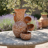 Decorative terracotta vase with floral patterns on a stone surface outdoors.