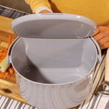 Gray two-tiered salad spinner on a wooden surface with a person wearing a yellow sweater in the background.