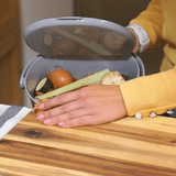 Person disposing of food waste into a compost bin on a wooden surface.