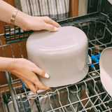 Person placing a white bowl into an open dishwasher.