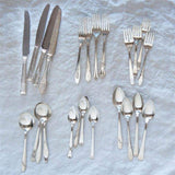 Collection of silver cutlery including knives, forks, and spoons on a textured surface.
