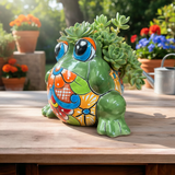 Colorful ceramic frog planter with succulents on a wooden table outdoors.