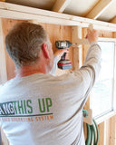 Person using a drill to assemble wooden shelves in a shed.
