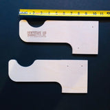 Two wooden wall hooks with 'Hang This Up' branding on a dark surface, measured by a tape measure.