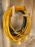 Coiled yellow extension cord on a wooden holder against a wall.